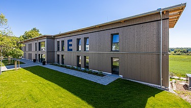 Außenansicht des Gebäudes mit Eingang und grauer Holzfassade